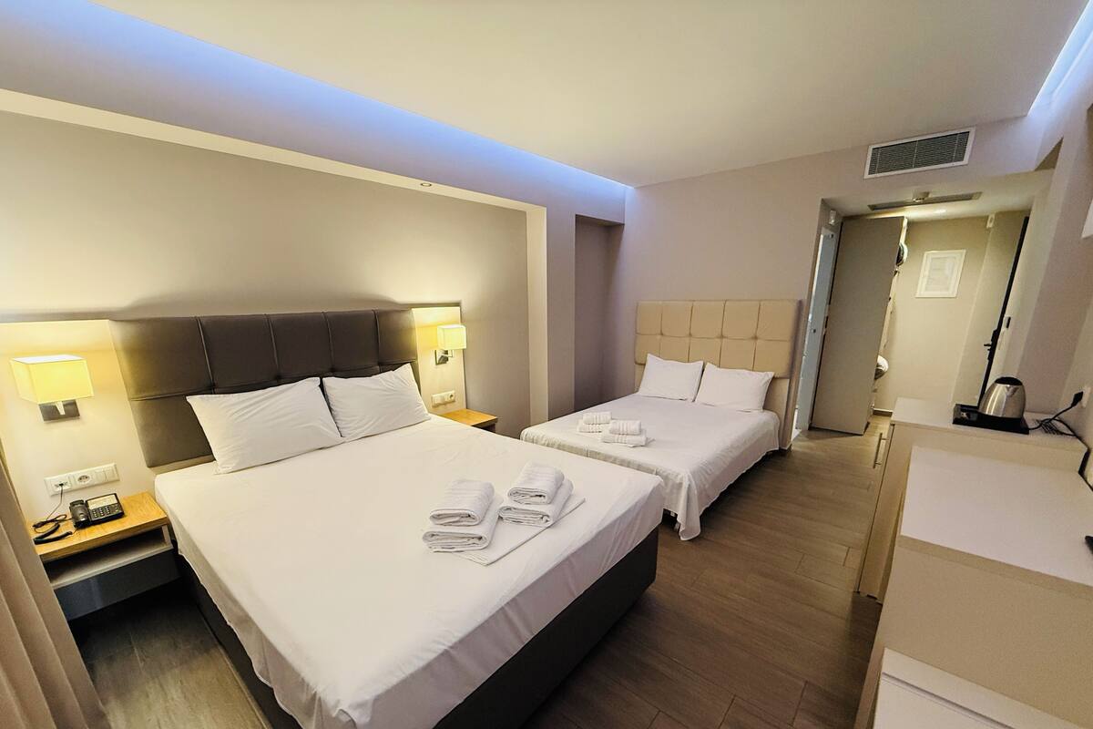 Habitación de hotel con dos camas, cada una con cabecero, lámparas de noche y toallas dobladas con cuidado.