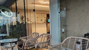 Un espace de détente intérieur moderne, avec des chaises en osier et une table ronde, agrémenté d’une cloison en verre et d’une horloge bien visible.