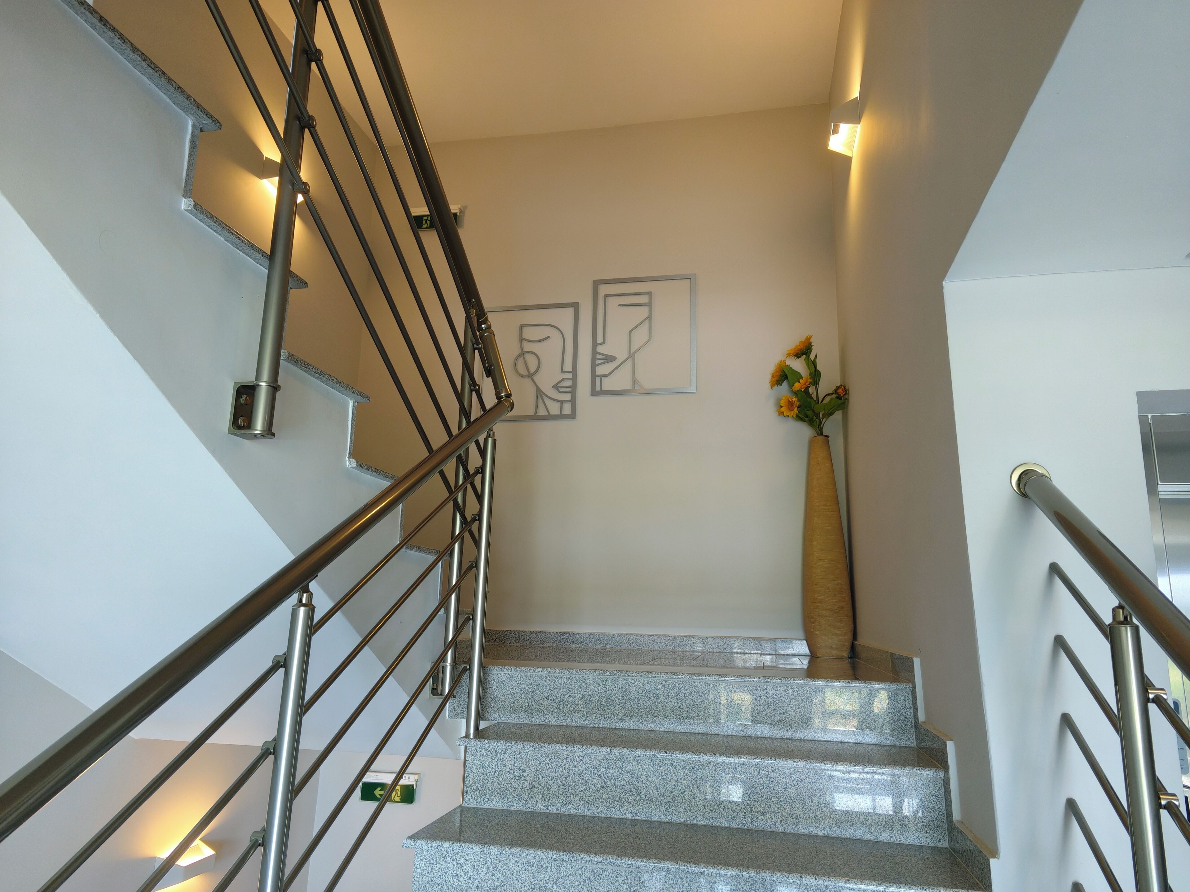 A staircase with metal railings and granite steps, a wall-mounted light, and a framed artwork.