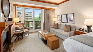 A hotel room with a sofa, armchair, coffee table, and a bed. There is a balcony with a view of buildings and trees. - #343 | Studio | NATIONAL | 3rd Floor Pool & Mountain Views (Stowe)