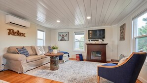 Una sala de estar con un sofá color beige, un sillón azul, una mesa de centro de madera, una chimenea y un televisor.