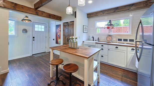 Una cocina con una isla de madera, armarios blancos, un refrigerador y luces colgantes.