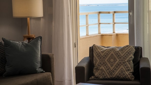 Una habitación con vista al mar, un sofá, una lámpara y un cojín estampado.