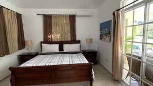 Een slaapkamer met een groot bed, een plafondventilator, een raam met gordijnen en uitzicht op de omgeving.