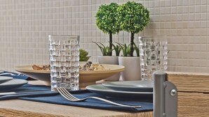 Een eettafel met glazen, borden en bestek, een potplant en een betegelde muur op de achtergrond.