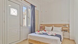 Een slaapkamer met een houten bed, wit beddengoed, een raam met uitzicht, een witte deur en een blauw gordijn.