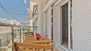 Een balkon met een houten tafel en stoelen, een rode koffiekop en een schuifdeur die naar een binnenruimte leidt.