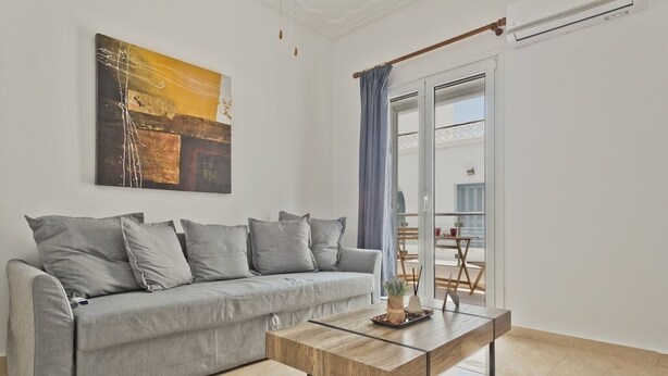 Een woonkamer met een grijze bank, een houten salontafel en een schilderij aan de muur.