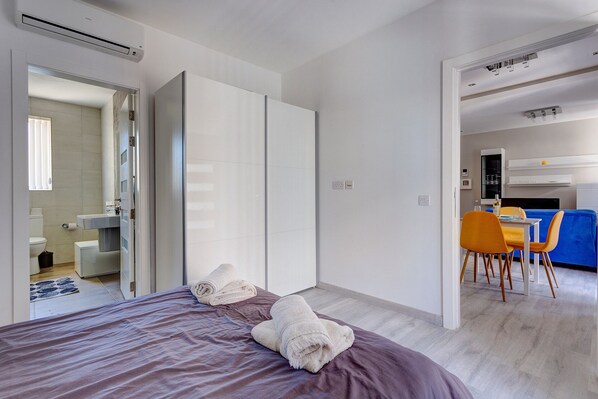 A modern hotel room with a bed, a bathroom, and a dining area.