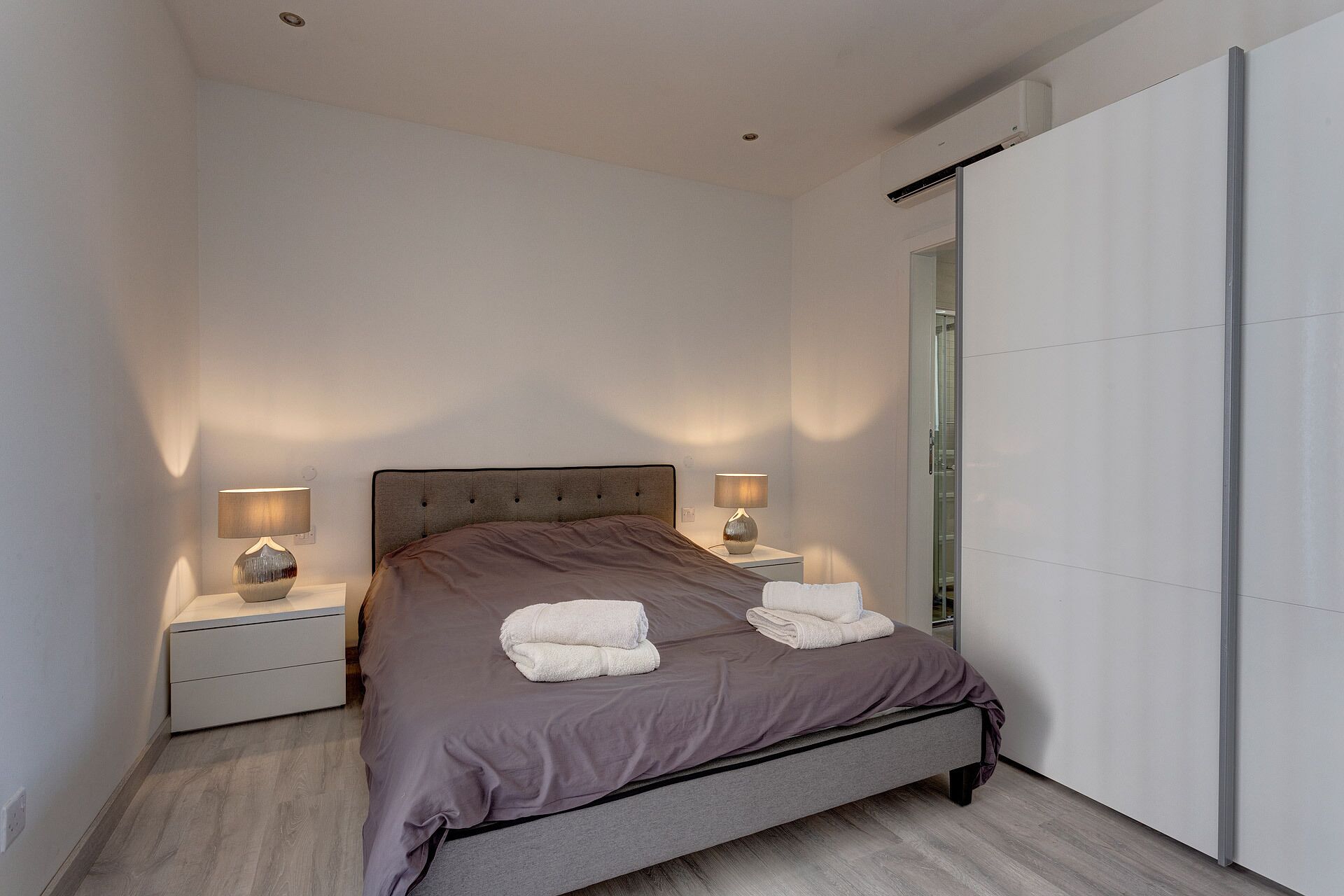 A modern bedroom with a bed, two bedside tables, and a large mirror.