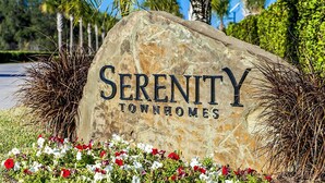 En stor stenskilte med ordene "Serenity Townhomes" i midten, omgivet af grønt og blomster.