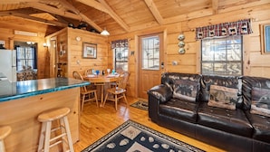 A cozy cabin interior with a wooden dining area, a leather sofa, and a bar with stools. - Forever Mine: A Romantic Escape for Two (Gatlinburg)