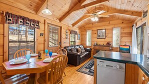 A cozy cabin interior with a wooden dining table, chairs, a leather sofa, and a kitchen area. - Forever Mine: A Romantic Escape for Two (Gatlinburg)