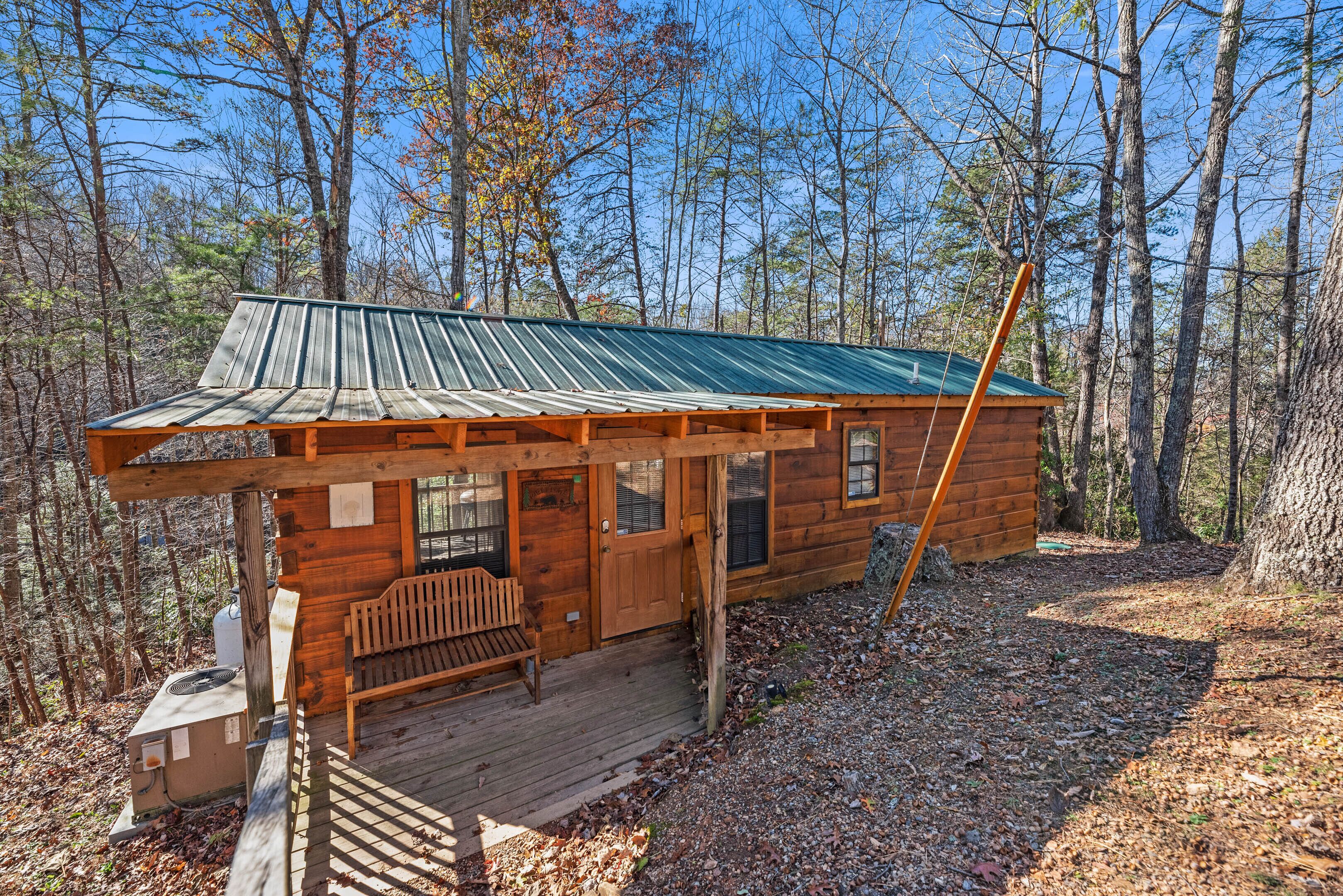 A wooden cabin with a metal roof, a wooden deck, and a bench.