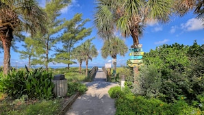Un sentier menant à une plage bordée de palmiers, avec un panneau indicateur indiquant les directions vers différentes attractions.