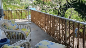 A balcony with wicker furniture and a bamboo fence, overlooking a lush garden.