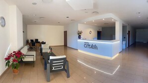 A hotel reception area with a modern design, featuring a reception desk, seating area, and a clock on the wall. - Città Della Notte (Melilli)