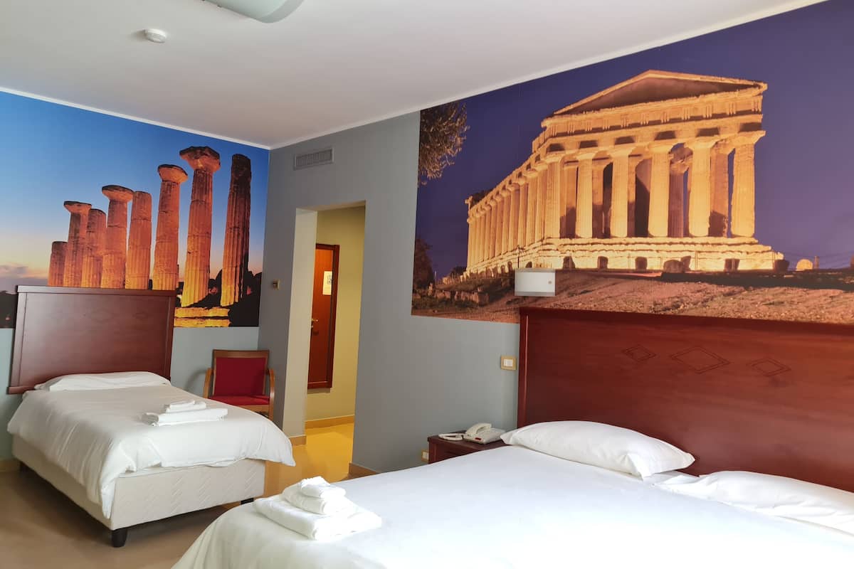 A hotel room with two beds, a mural of ancient columns, and a large painting of a classical building.