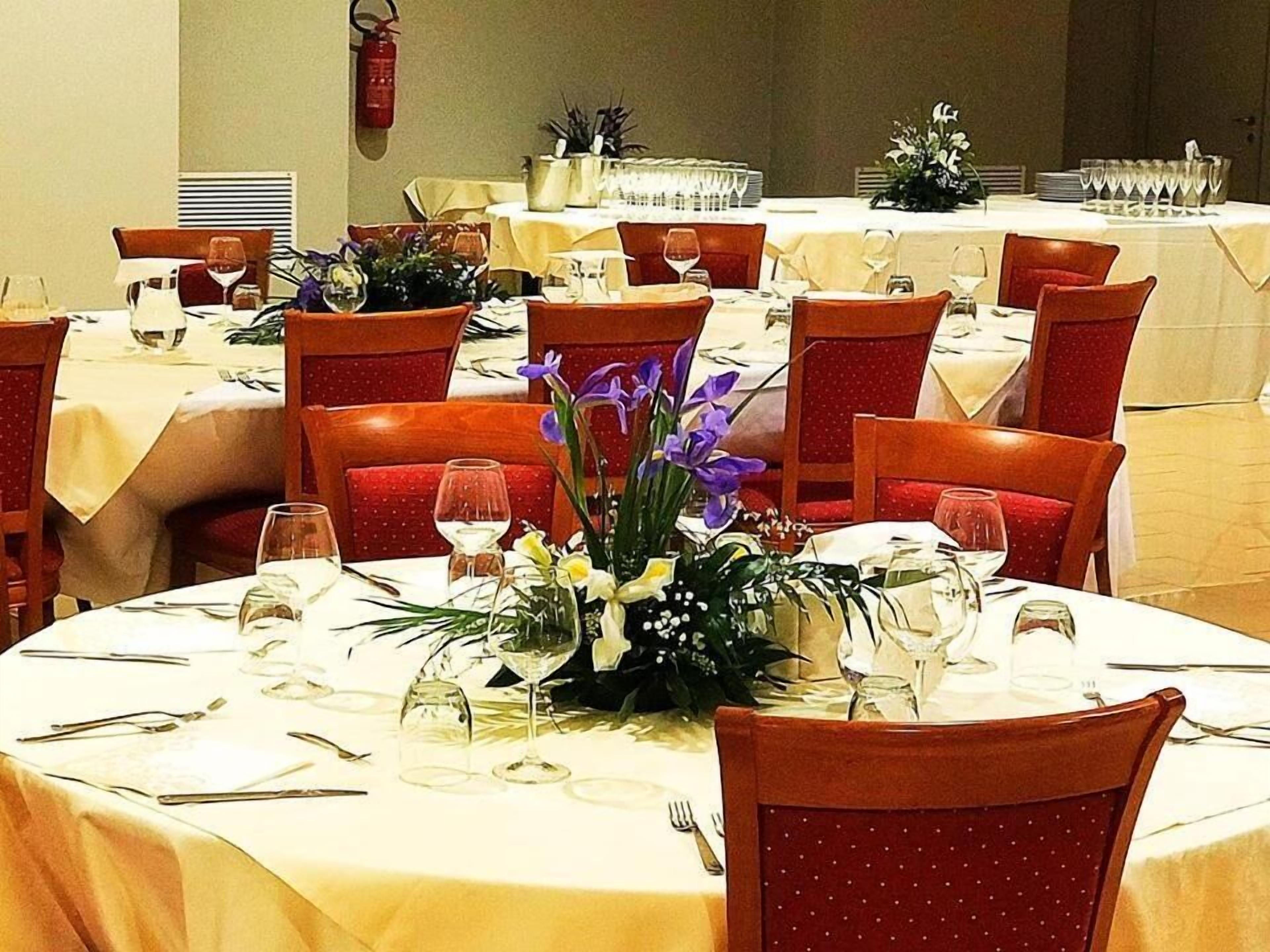 A dining area with round tables, red upholstered chairs, and white tablecloths.