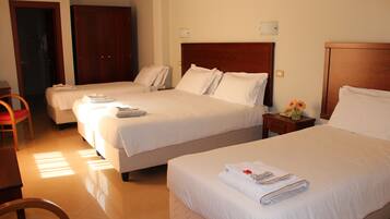 A hotel room with two beds, a wooden wardrobe, a small table with a vase, and a chair.
