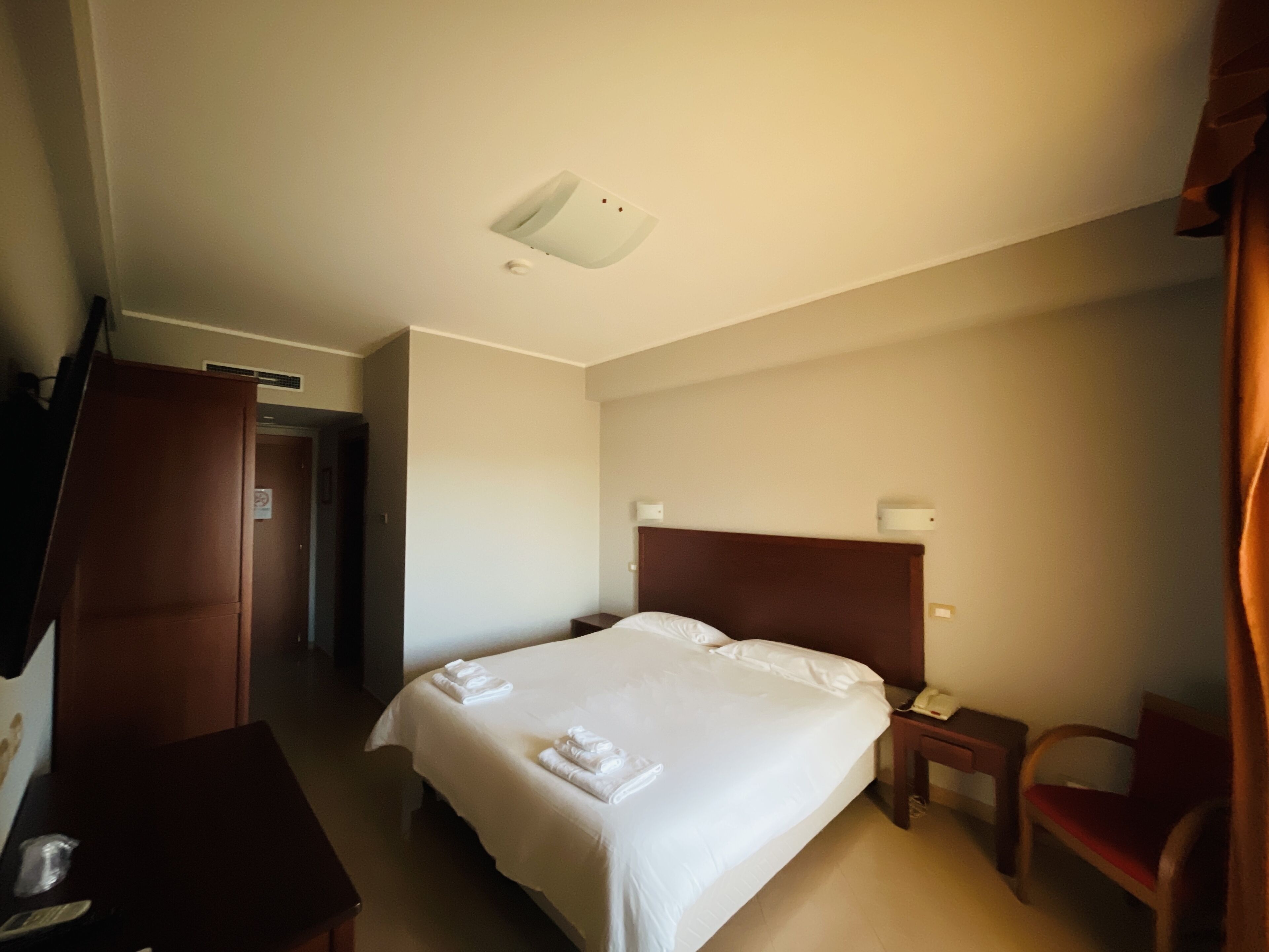 Habitación de hotel con cama, escritorio, silla, mesita de noche y puerta.