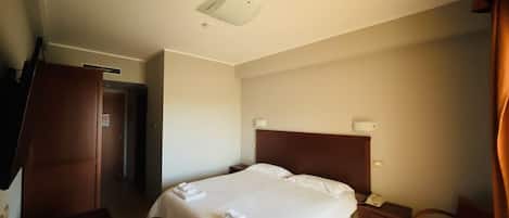A hotel room with a bed, a desk, a chair, a bedside table, and a door.