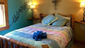 Un dormitori amb un llit, un capçal de fusta, dues làmpades penjades a la paret, una decoració de branca i una finestra.