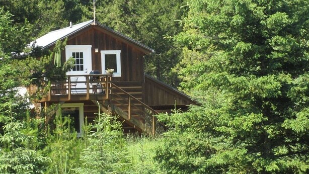 Una cabana de fusta amb un balcó, envoltada per un bosc dens.