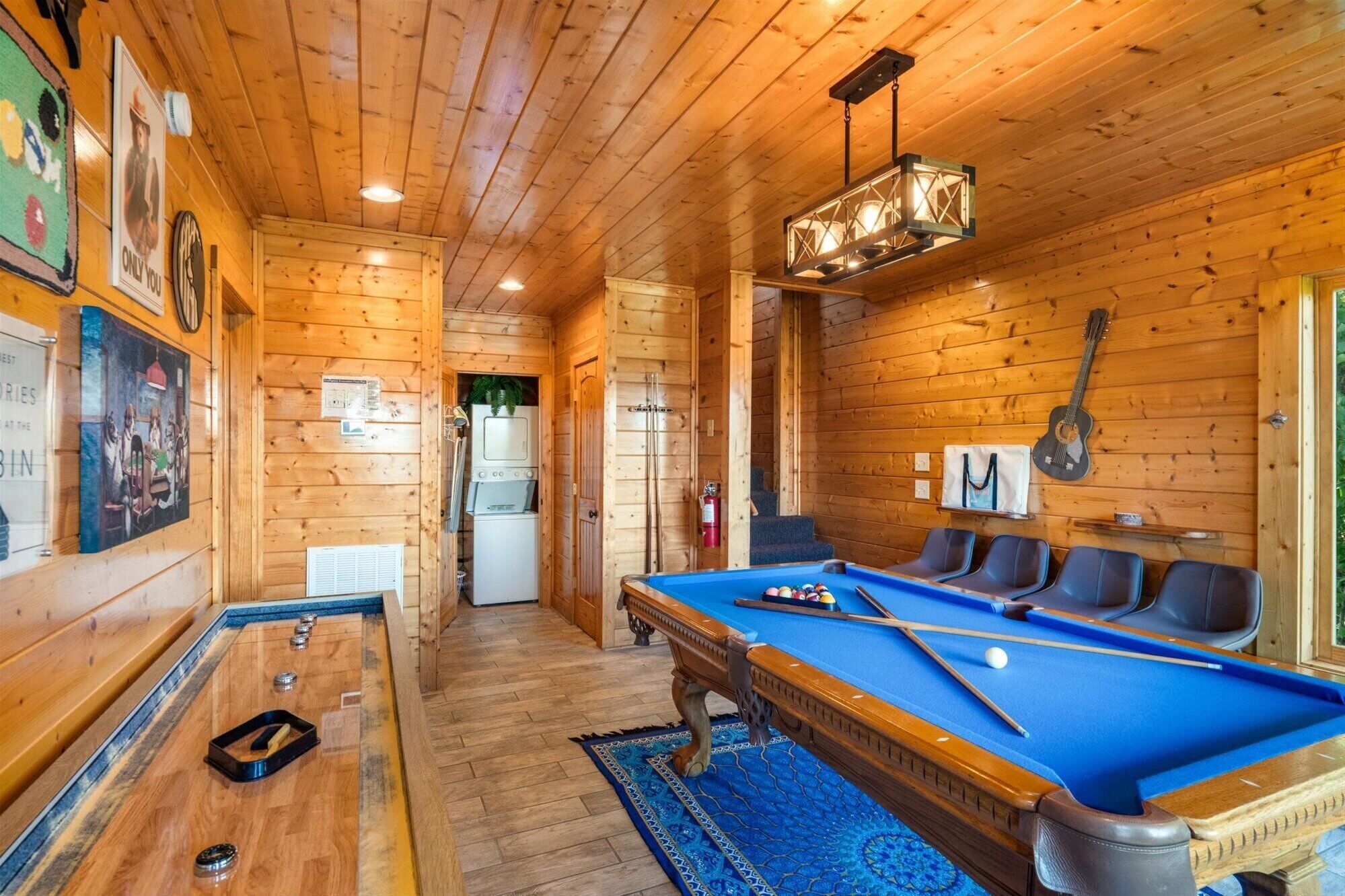 A cozy wooden cabin with a pool table, a refrigerator, and a guitar on the wall.