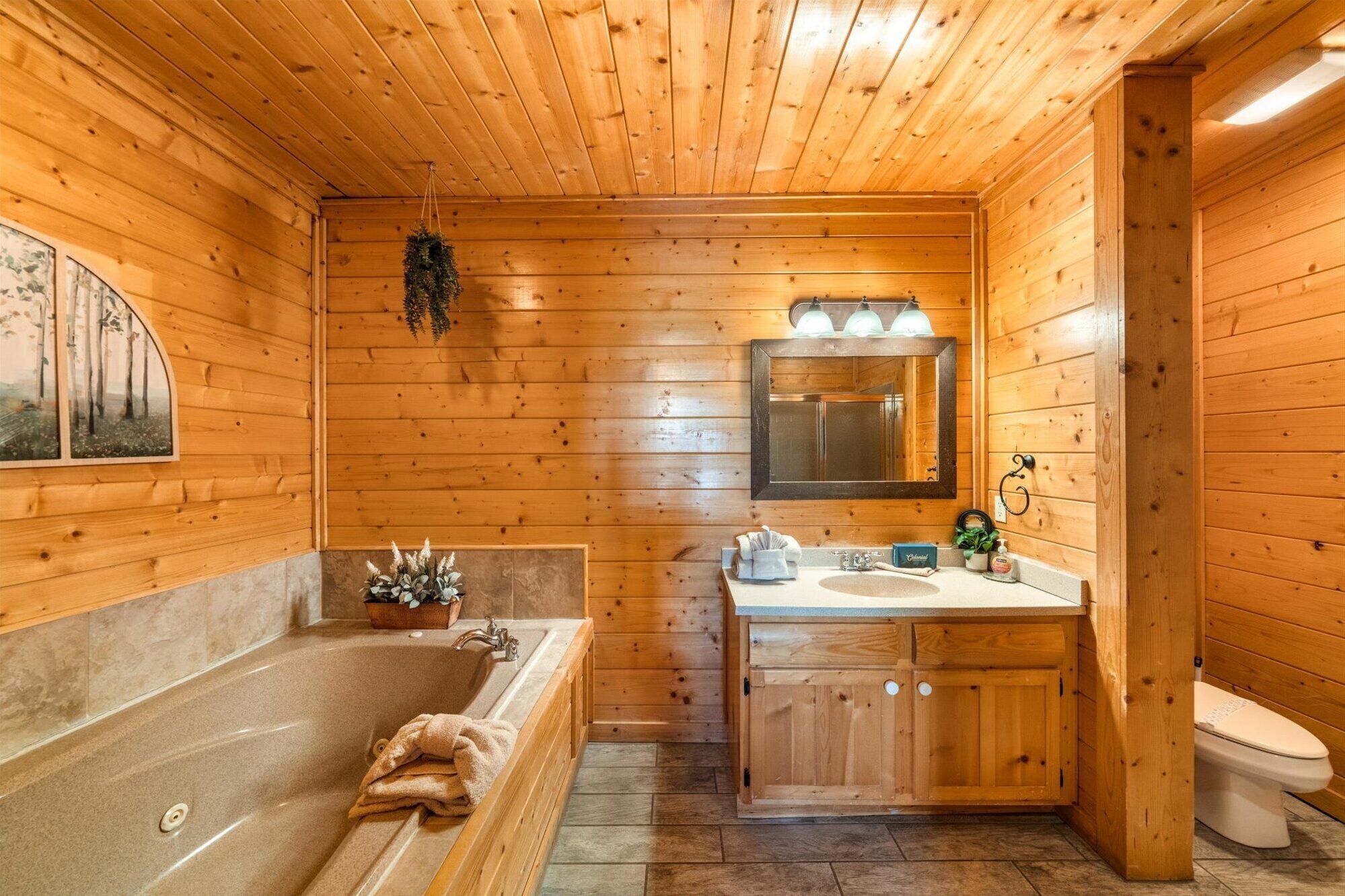Une salle de bain rustique, aménagée dans une cabane en bois, avec une baignoire, un lavabo et des toilettes.