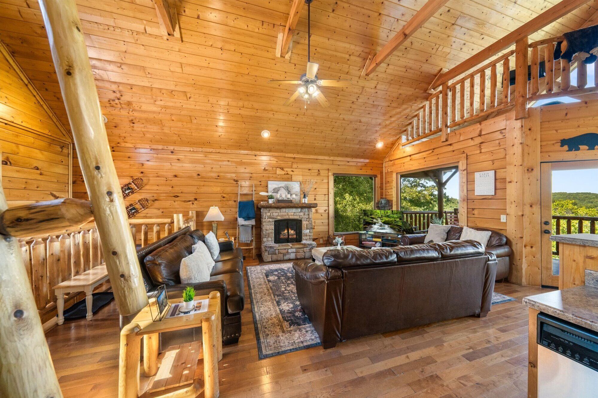 A log cabin interior with a fireplace, leather furniture, and a balcony with a view.