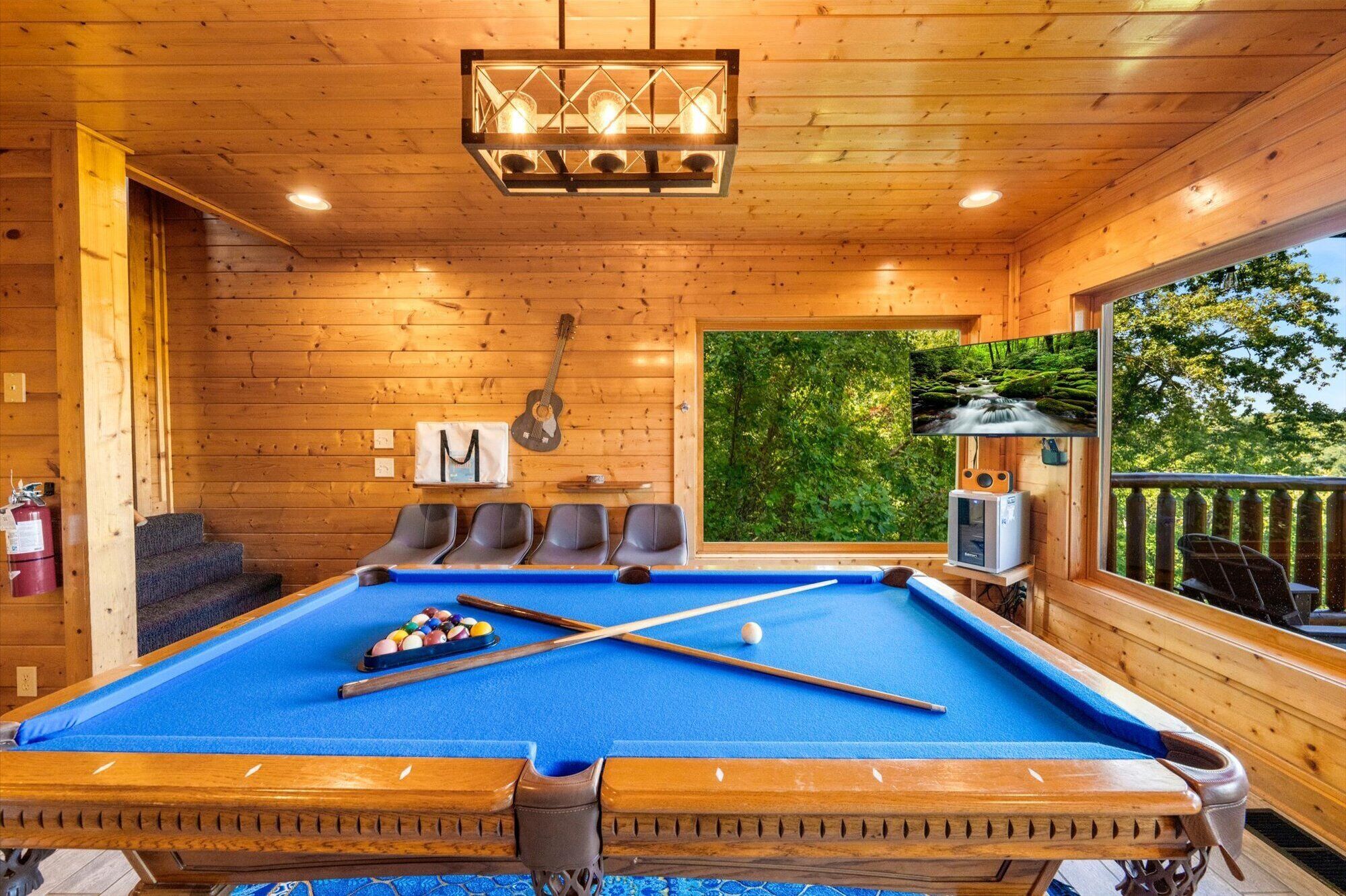 Une cabane en bois équipée d’une table de billard, de chaises, d’une guitare et d’un téléviseur.