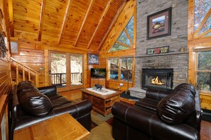Un intérieur de chalet chaleureux avec une cheminée, des canapés en cuir et un manteau de cheminée en pierre.