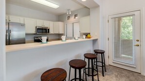 Une cuisine moderne avec des meubles blancs, des appareils en acier inoxydable et un coin bar équipé de tabourets.