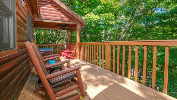 A wooden deck with a rocking chair and a table, overlooking a forested area. - Smoky Mountain High: Where the Mountains Lift You (Gatlinburg)