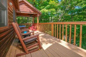A wooden deck with a rocking chair and a table, overlooking a forested area.