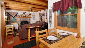 A cozy cabin interior with a wooden dining table, a brown sofa, and a fireplace. - Smoky Mountain High: Where the Mountains Lift You (Gatlinburg)