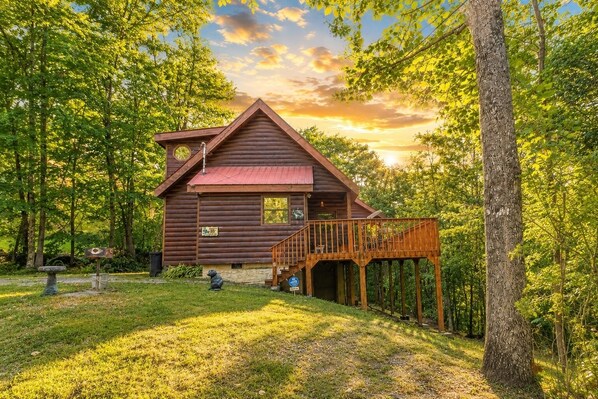 A wooden cabin with a deck, surrounded by trees.