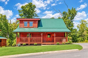 A log cabin with a green roof, a porch with railings, and a well-maintained lawn.