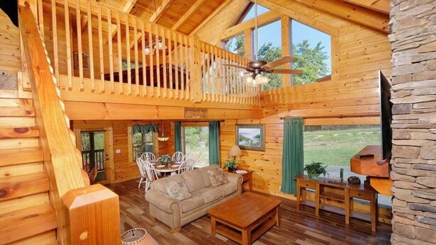 A spacious wooden cabin with a loft bedroom, a cozy living area with a sofa and coffee table, and a stone fireplace.