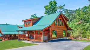 A log cabin with a green metal roof, a front porch, and a stone foundation.