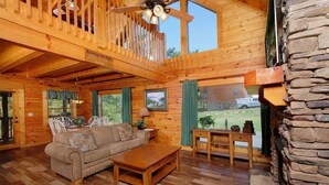 A wooden cabin interior with a wooden ceiling, a stone fireplace, a dining area, and a sofa.
