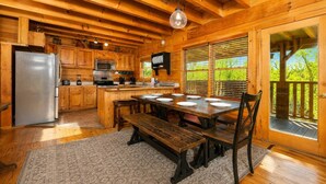 A wooden cabin with a kitchen, dining area, and a deck with a view of greenery. - Deer Lodge: Putt, Play & Take in the Views (Pigeon Forge)
