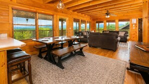A wooden cabin interior with a dining table, benches, a sofa, and a ceiling fan. - Deer Lodge: Putt, Play & Take in the Views (Pigeon Forge)