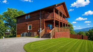 A two-story wooden cabin with a balcony, a driveway, and a well-maintained lawn. - Deer Lodge: Putt, Play & Take in the Views (Pigeon Forge)