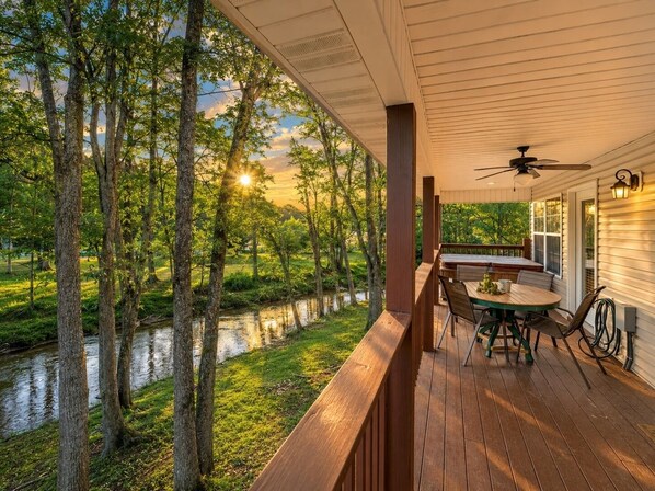Una terraza de madera con una mesa y sillas, con vistas a un río y árboles.