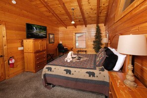Ein gemütliches Blockhauszimmer mit Bett, Fernseher, Kamin und Weihnachtsbaum.