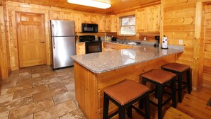 Cocina de cabaña de madera con encimera de granito, refrigerador, microondas, estufa y taburetes de bar.