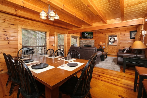 A wooden cabin interior with a dining area, a fireplace, and a living room.