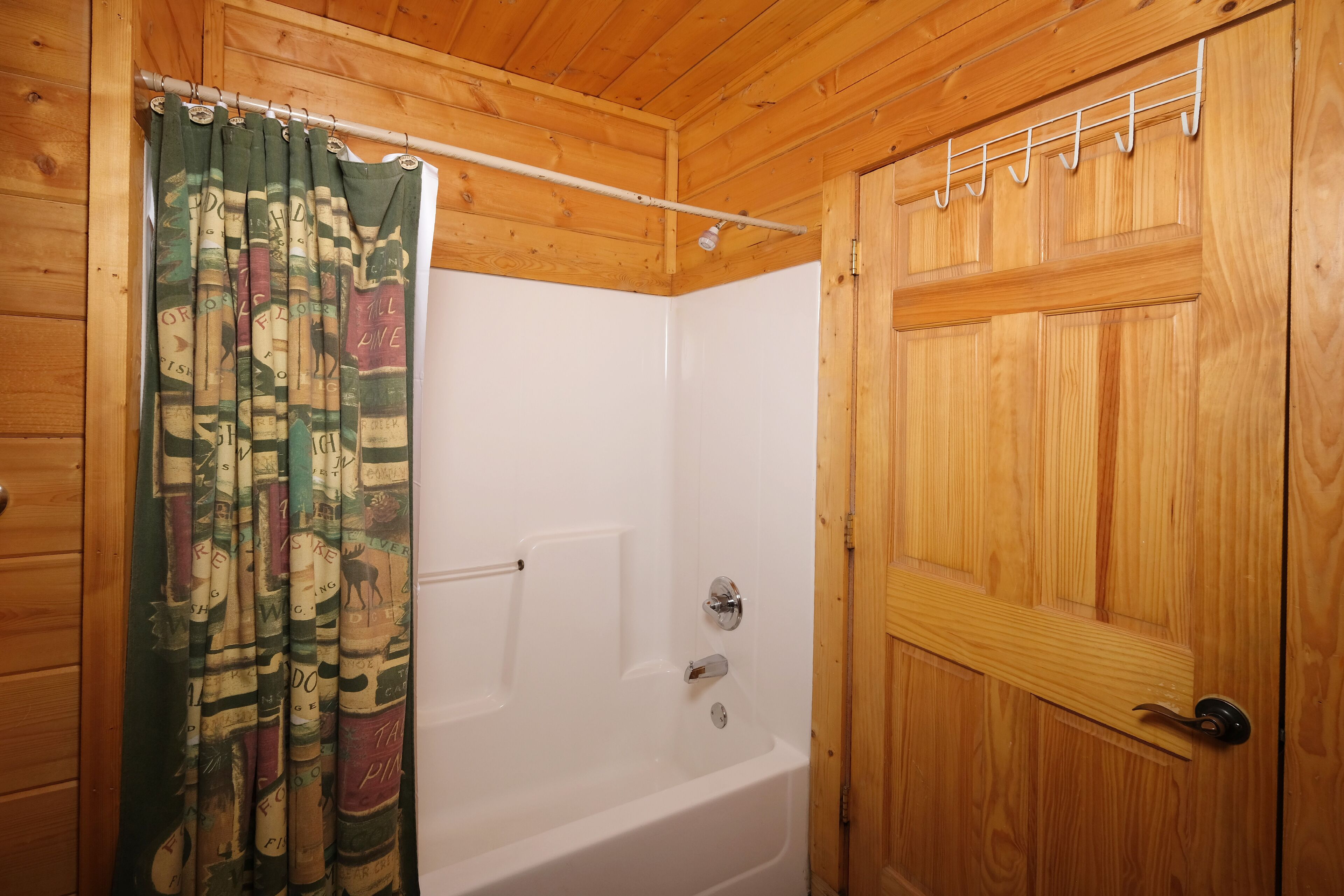 Casa de banho de cabana de madeira, com uma banheira branca, porta de madeira e cortina de chuveiro com estampas de animais.